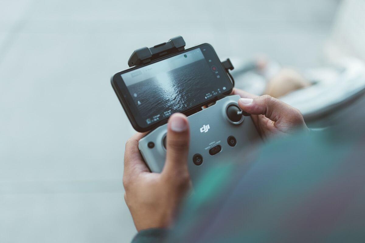Mains tenant une manette de jeu DJI avec un smartphone fixé dessus.