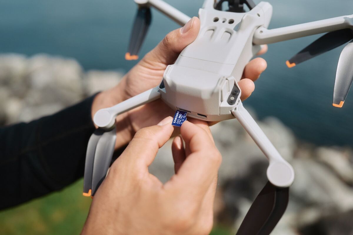 Mains tenant un drone blanc avec une carte mémoire insérée.