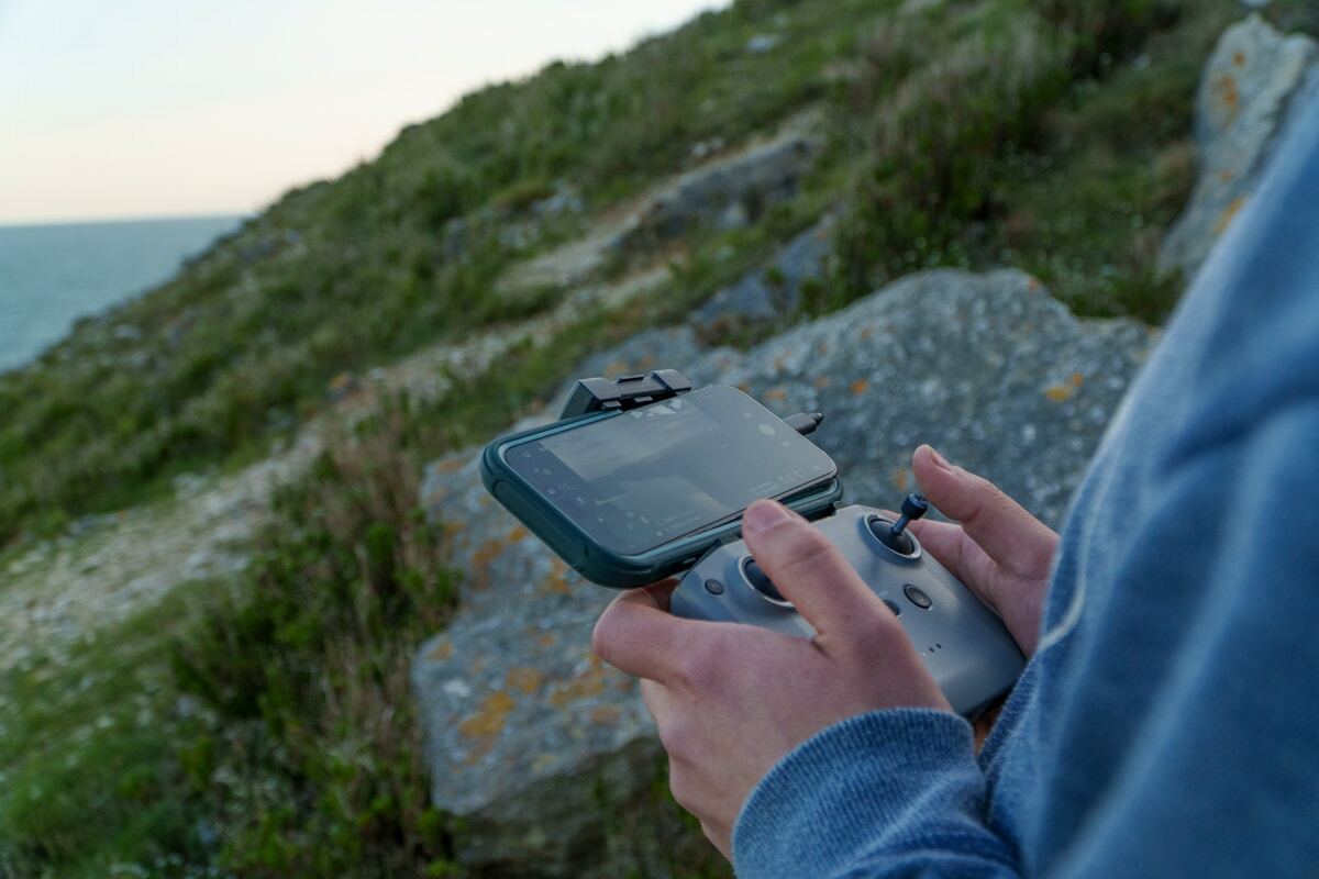 Personne tenant une manette de jeu vidéo avec un paysage naturel en arrière-plan.