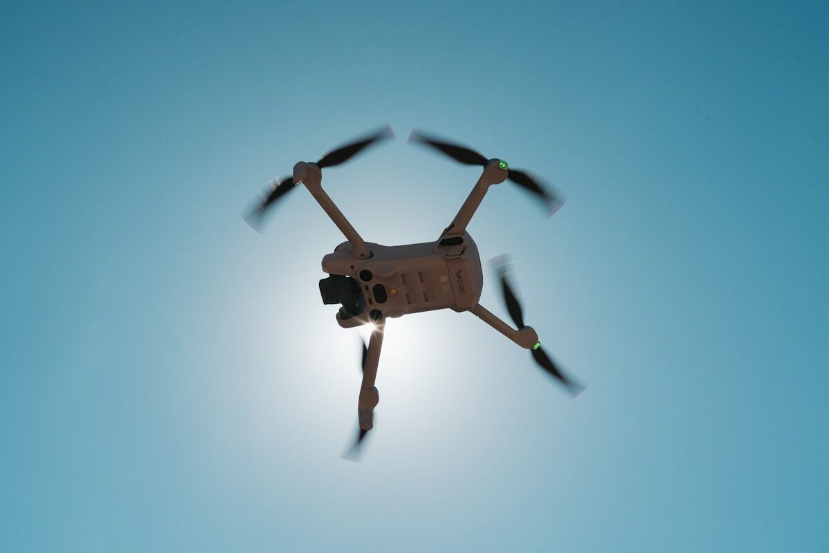 Drone volant avec hélices en mouvement sur fond bleu clair.