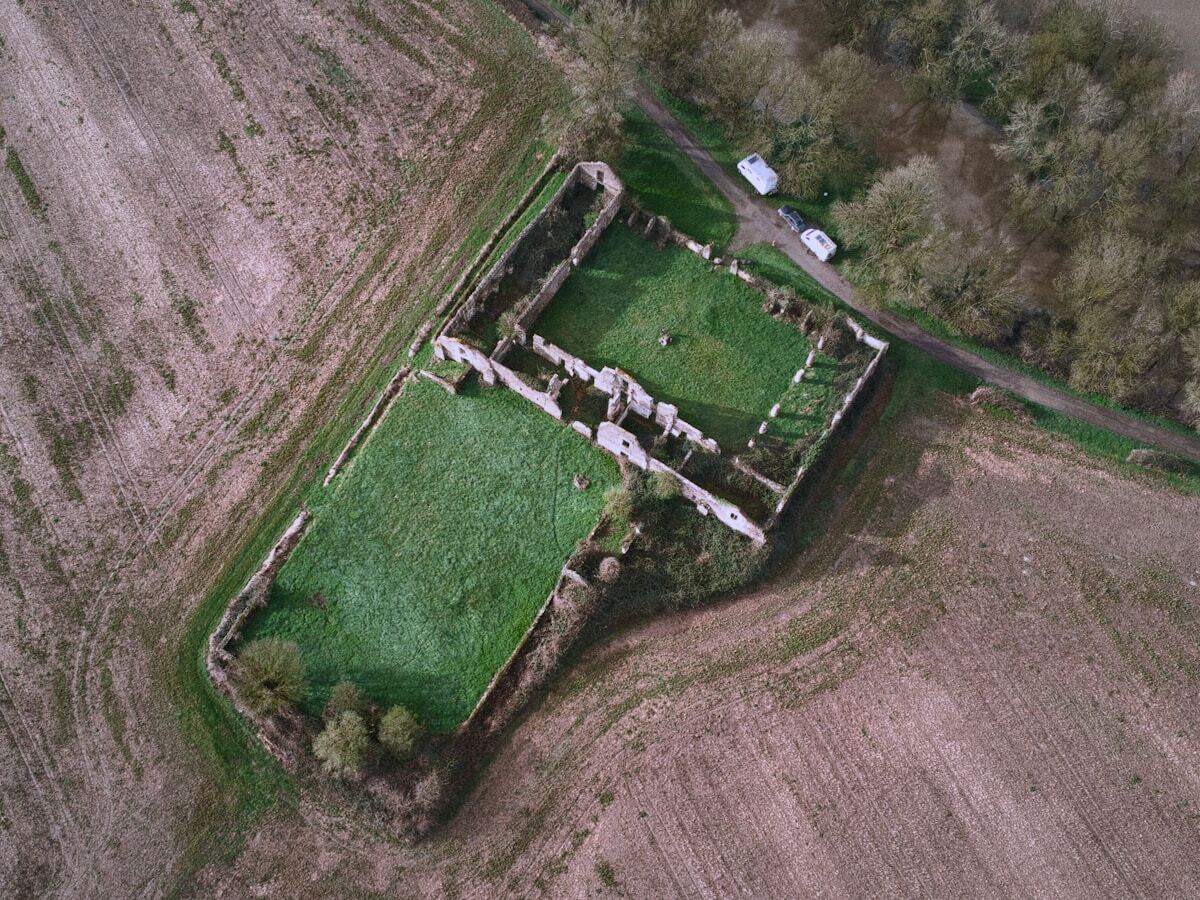 Ruines d'un ancien bâtiment entouré de champs et de végétation.