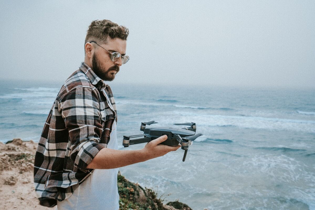 Homme barbu tenant un drone au-dessus de l'océan.