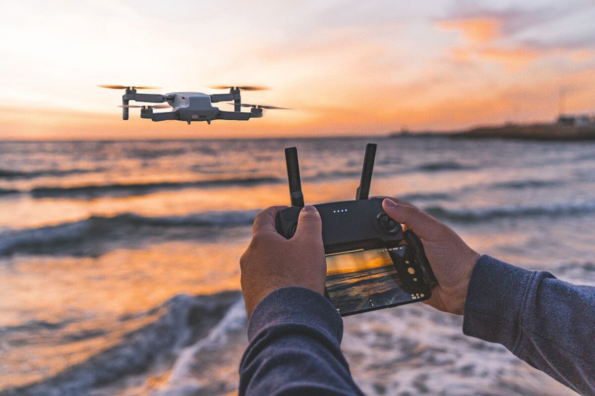 Drone volant au-dessus de l'océan au coucher du soleil, contrôlé par une personne.