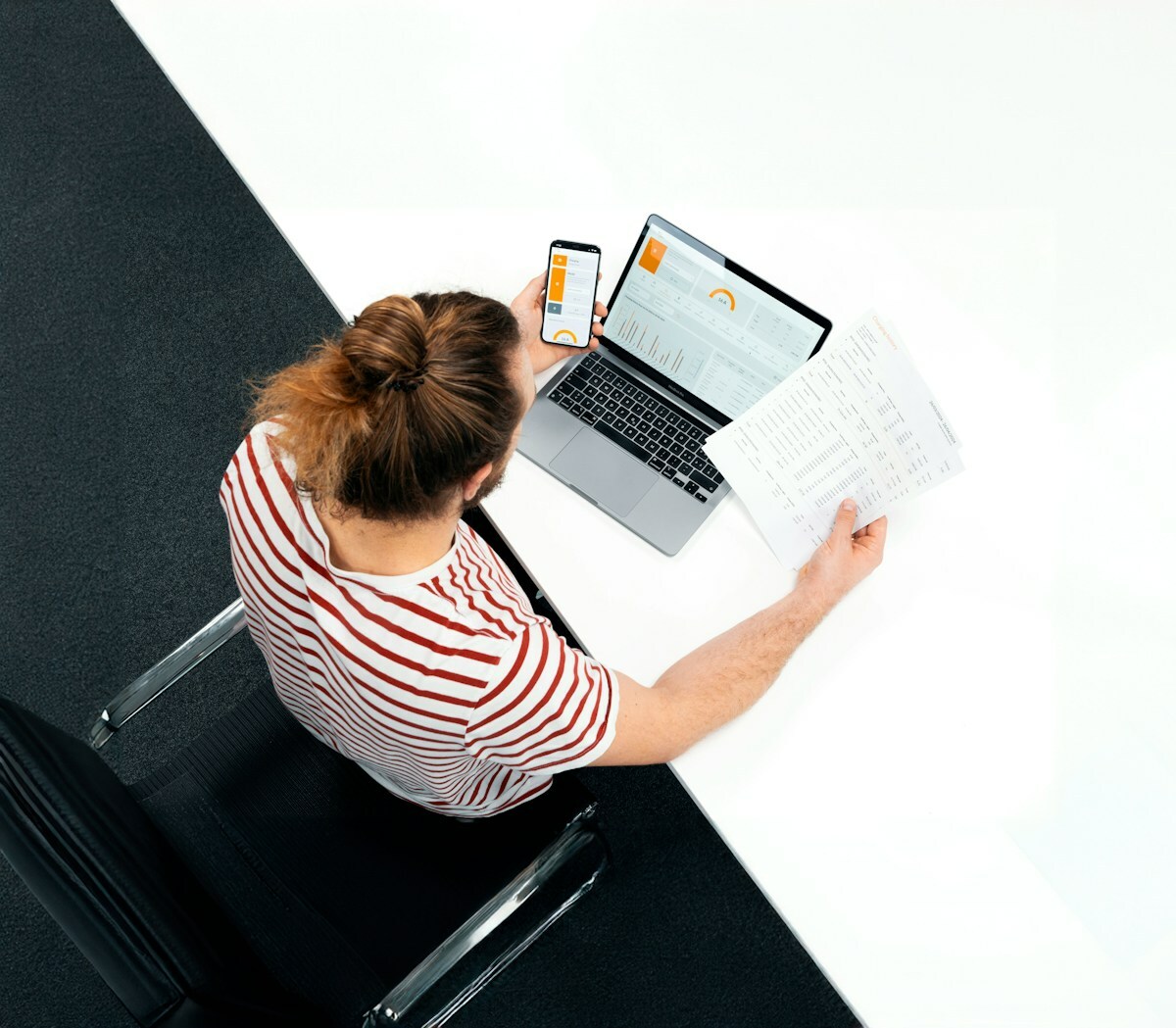 Femme travaillant sur ordinateur portable et smartphone, documents papier.