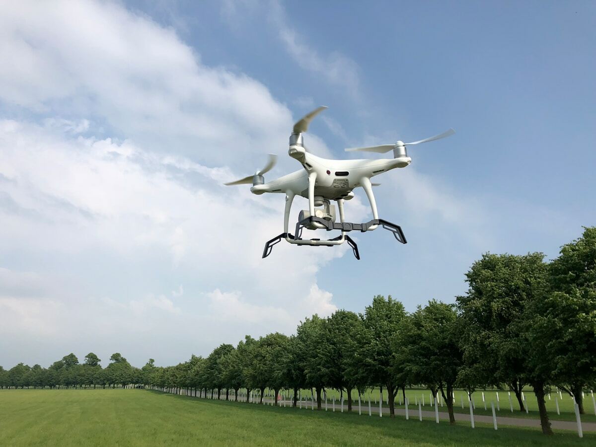 Drone blanc volant au-dessus d'un cimetière militaire avec des arbres.