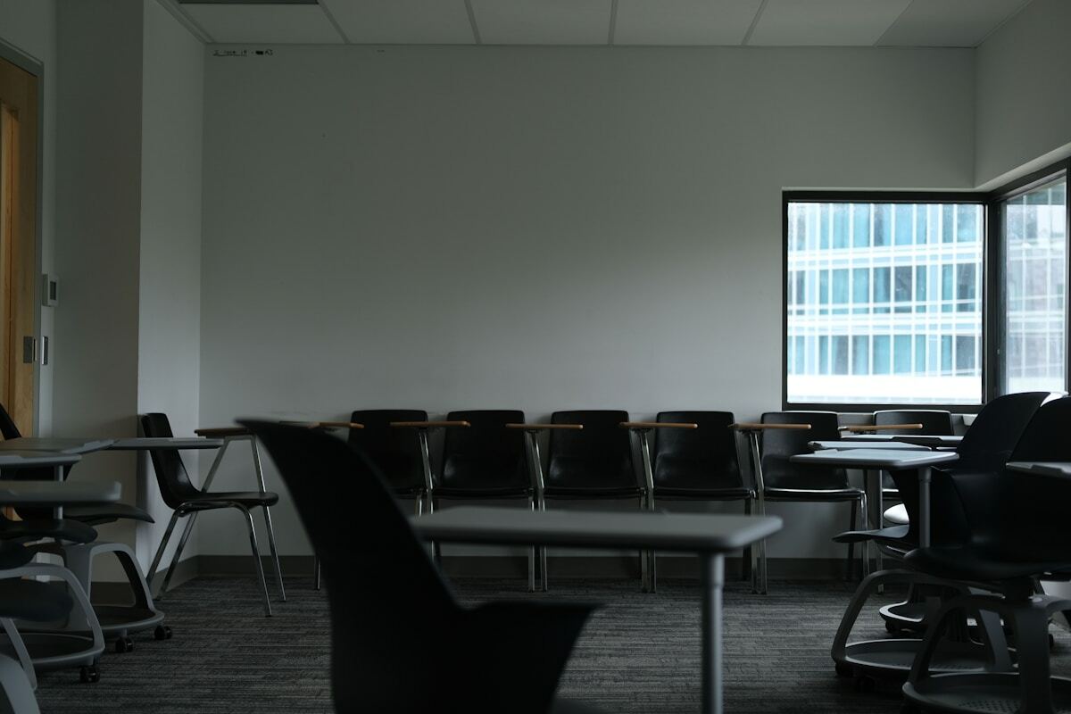Salle de classe vide avec des tables et des chaises noires.